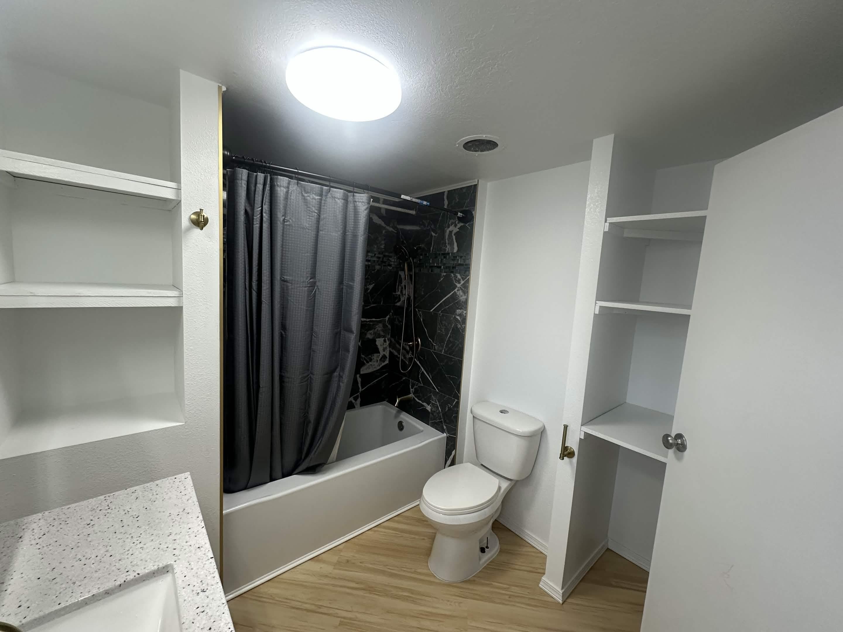 Remodeled bathroom with black marble tub surround, white vanity, and quartz countertop