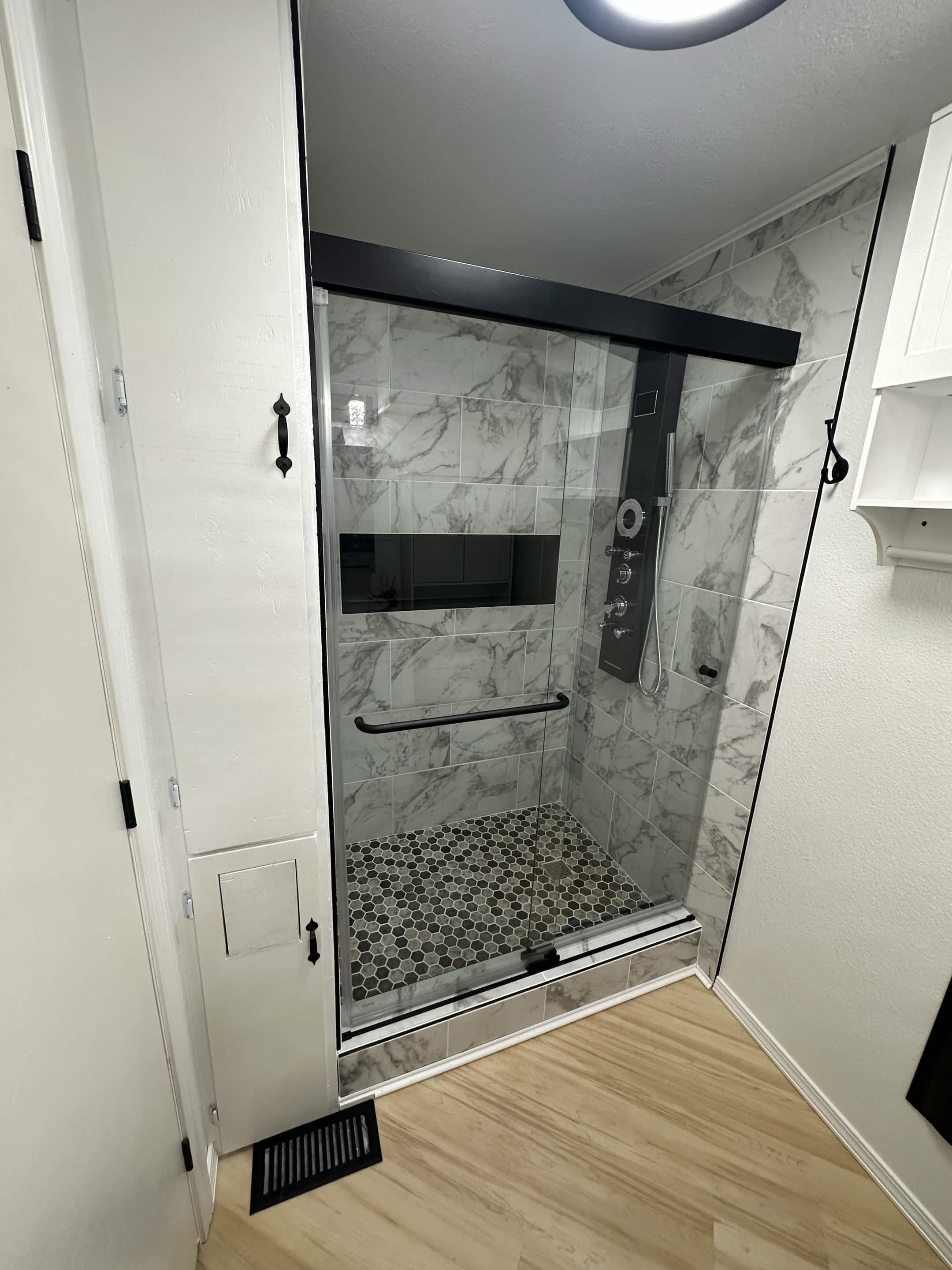 Walk-in shower with white marble tile, glass doors, and hexagon mosaic floor