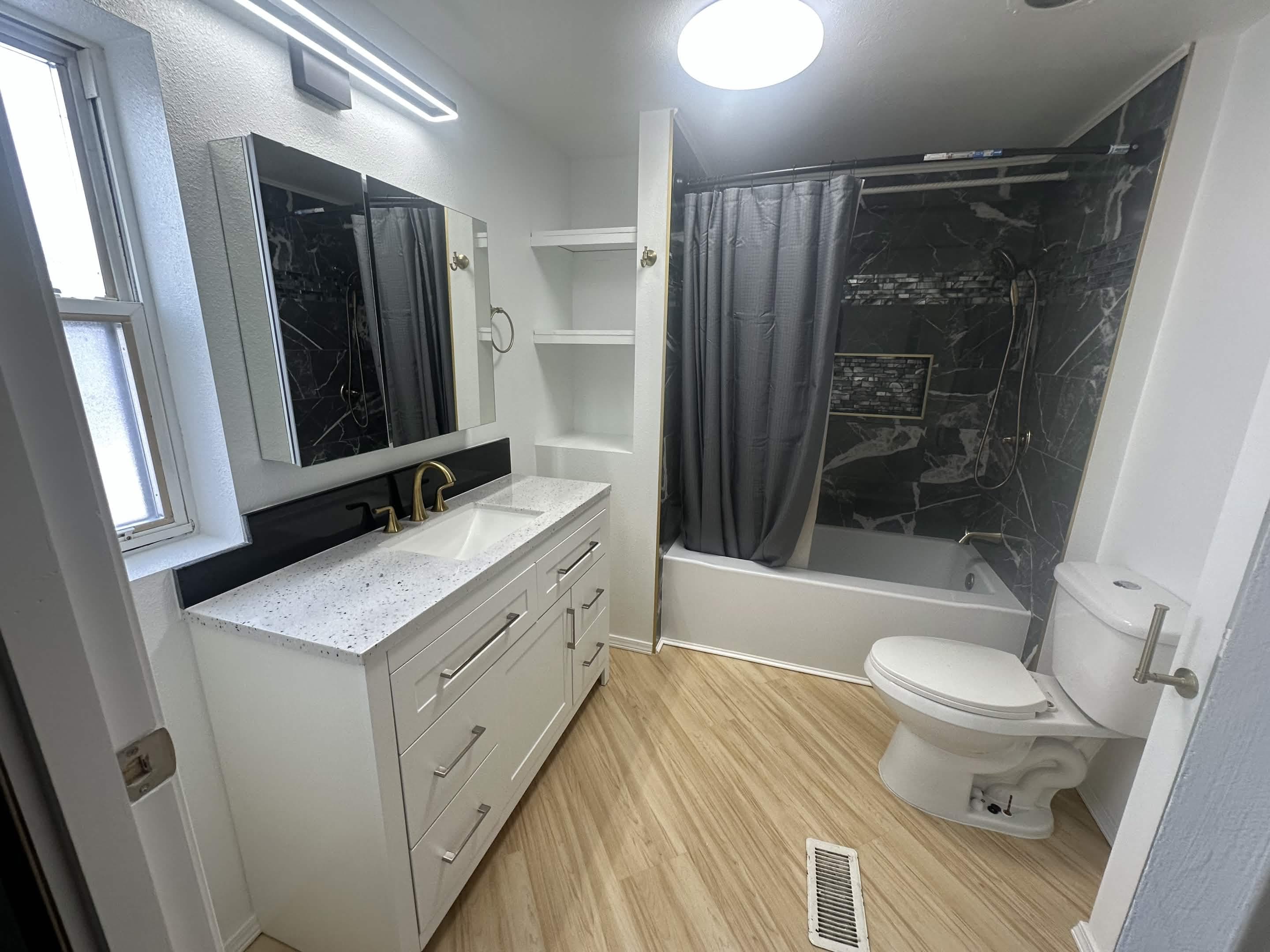 Bathroom after remodel — modern white vanity, quartz countertop, and black marble shower